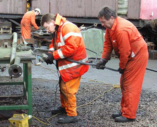 John Salter holds a piece of brake pipe whilst Kevin Blake wire brushes it. In the background Leon Salter is also working on some brake pipe work. January 10 2004