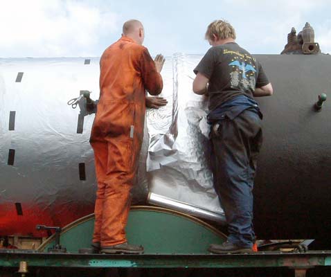 Steve Underhill (left) and Huw Button work at fitting the first layer of insulation - a layer of heavy duty aluminium foil. This should not only improve insulation but will also keep the potentially wet Kaowool away from direct contact with the boiler barrel. So we hope it will be less corroded the next time it all comes apart ! May 23 2004 &copy; Colin Henderson.