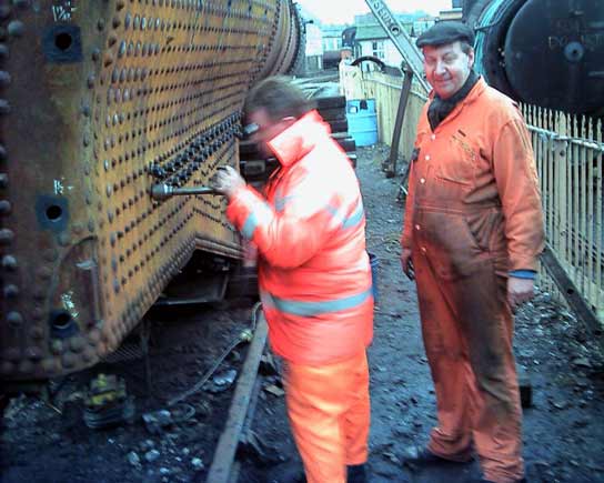 I don't think Dave Fuzard can quite believe how fast Kevin Blake is working. In something of a blur Kev cleans up the threads of the studs used to mount the firebox slides. March 8 2003 &copy; John Salter