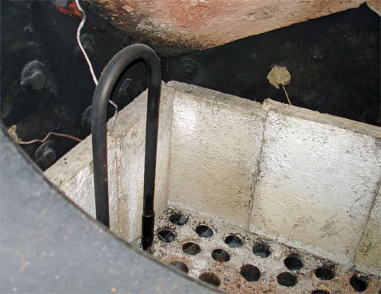 A view into the firebox. At the top can be seen the combustion arch. Below this on the blackened walls of the firebox are several thermocouples attached during the testing, tuning and acceptance process. Prominent is one of the pair of atomising steam superheater elements. The other is in the mirror image position. Note the double-wall thickness close to the panplate where the elements are directly in contact with flames. As can be seen the panplate itself is filled with fireclay. © Nigel Day