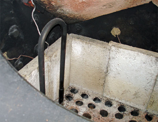 A view into the firebox. At the top can be seen the combustion arch. Below this on the blackened walls of the firebox are several thermocouples attached during the testing, tuning and acceptance process. Prominent is one of the pair of atomising steam superheater elements. The other is in the mirror image position. Note the double-wall thickness close to the panplate where the elements are directly in contact with flames. As can be seen the panplate itself is filled with fireclay. © Nigel Day A view into the firebox. At the top can be seen the combustion arch. Below this on the blackened walls of the firebox are several thermocouples attached during the testing, tuning and acceptance process. Prominent is one of the pair of atomising steam superheater elements. The other is in the mirror image position. Note the double-wall thickness close to the panplate where the elements are directly in contact with flames. As can be seen the panplate itself is filled with fireclay. © Nigel Day