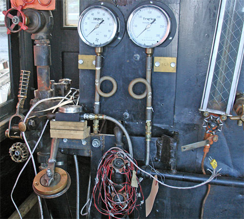 This is what the fireman sees. Towards the bottom left is the fuel flow control valve. Above this are the gauges showing the atomising steam pressure and blower pipe pressure. The atomising steam control valve is located above the gauge, out of view in this image. This photograph was taken during the early days of testing hence the coil of cables and the gauge sat on wooden blocks above the fuel flow valve. © Nigel Day